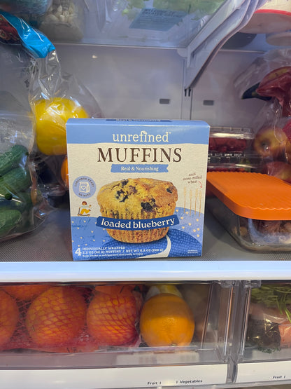 Box of blueberry muffins in a grocery store produce section with fruits and vegetables.