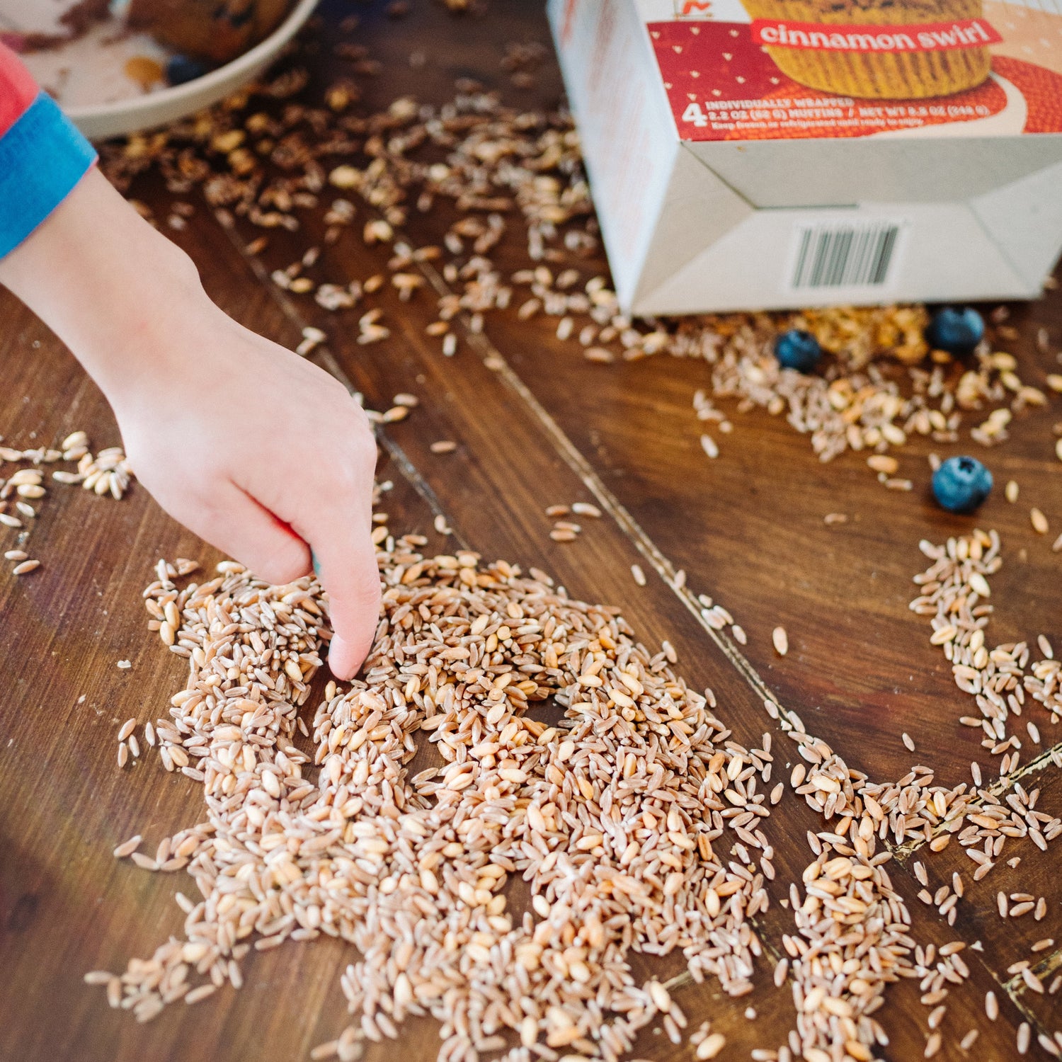 child drawing smiley face in a pile of whole grains with cinnamon swirl muffin in background